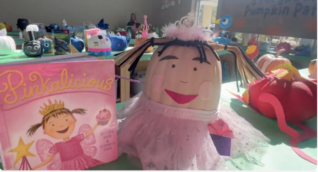 Picture from the video of a pumpkin painted to look like Pinkalicious next to the book, Pinkalicious. 