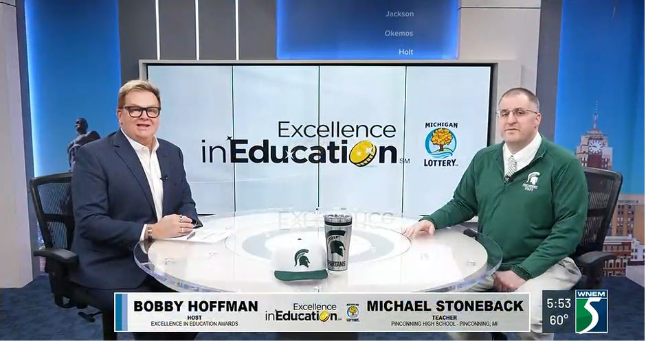 Mike Stoneback at a table with interviewer with spartan hat and cup on the table.