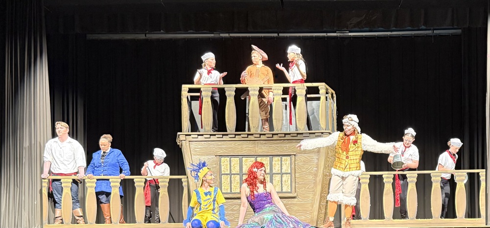 Actors on stage in front of a boat in the Little Mermaid