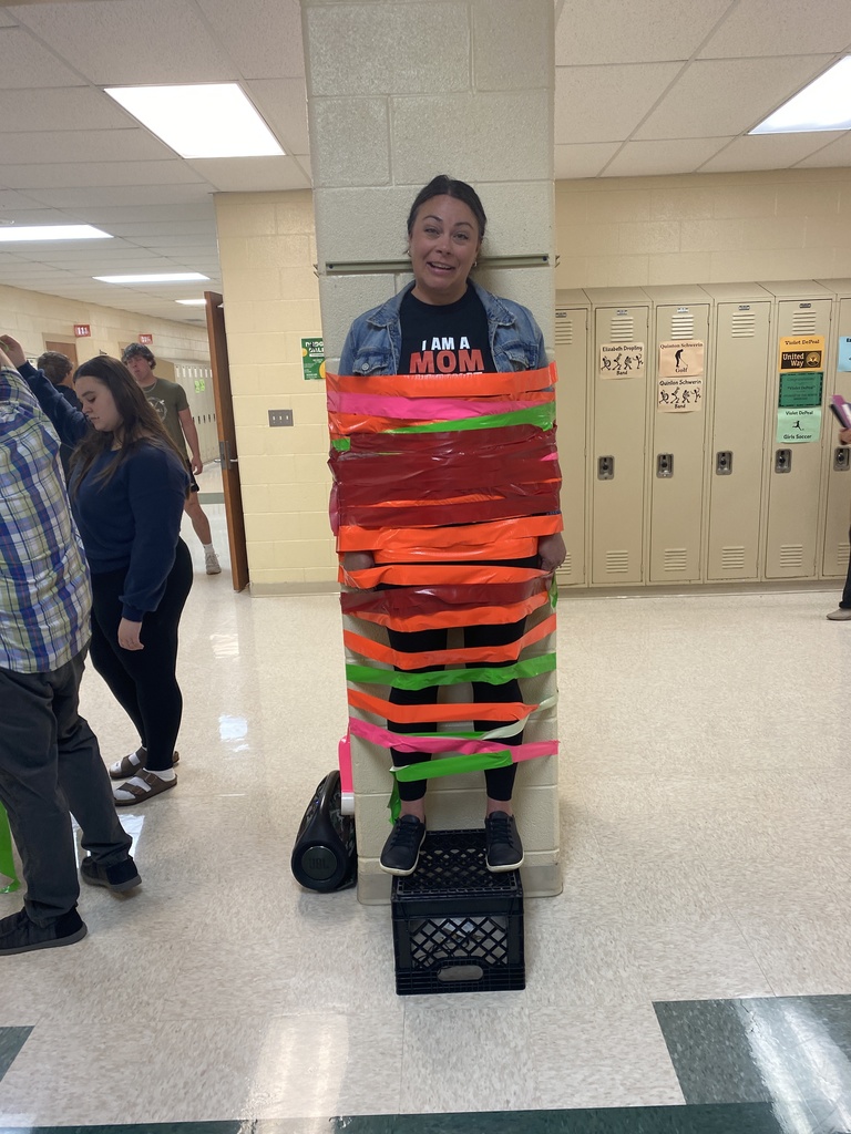 Mrs. Jaime standing on a crate taped to a column by colorful duct tape.