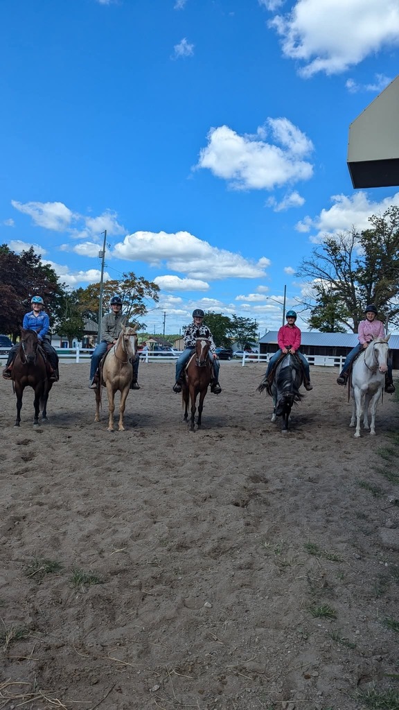 5 riders sitting on horses in a dirt arena.