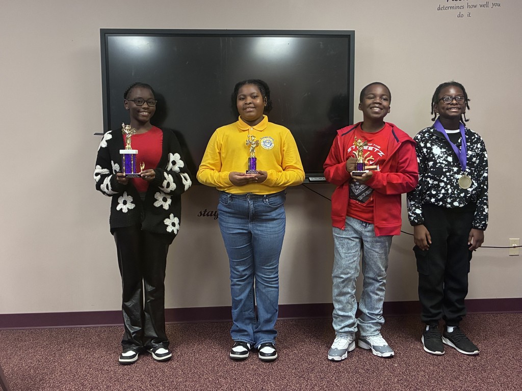 Four young people stand next to each other in front of a screen, holding awards.