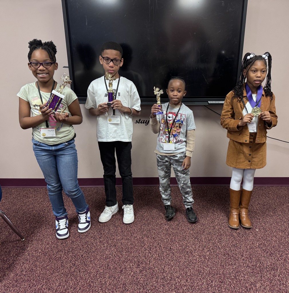 Four children in a room hold awards. They stand near a mounted TV screen and a white wall.