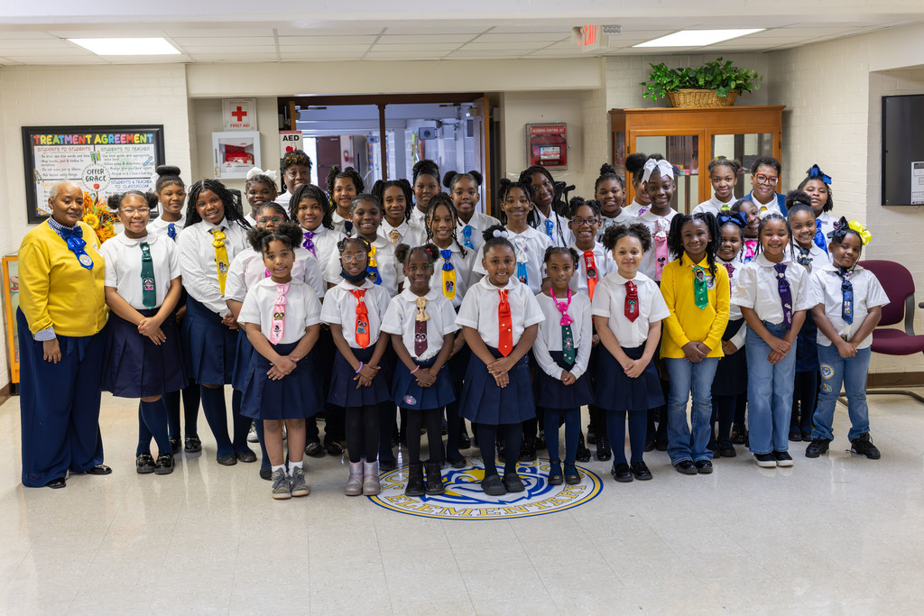 Group of students and staff in uniforms, some with ties, standing in a line.