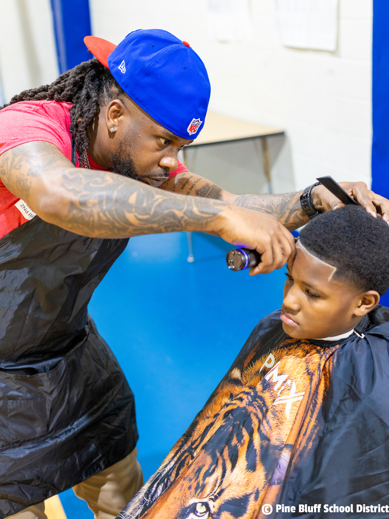 A person in a black apron cuts the hair of a young boy in a tiger-print cape.