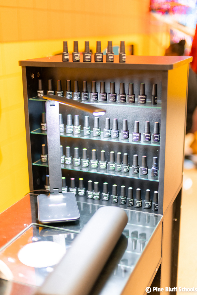 A wooden display cabinet with many bottles of nail polish. A lamp is on the countertop in front.