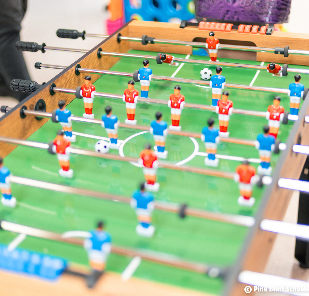 A close-up view of a table soccer game with miniature players in blue and red uniforms on a green field.