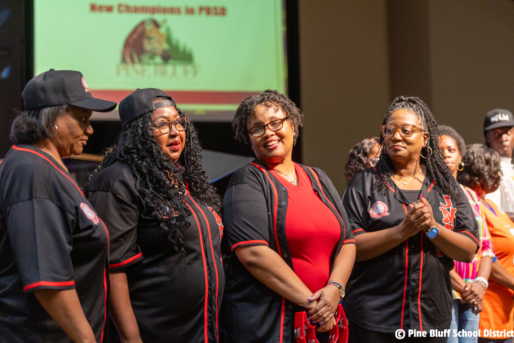 Five women stand together, wearing black tops with red and black trim, on a stage. A screen displays the text "New Champions in PSA".