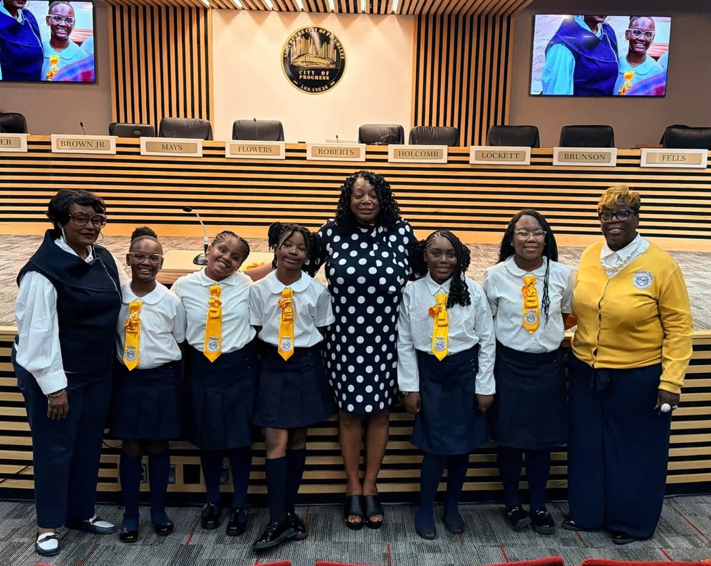 A group of women and children in uniforms pose in front of a council chamber.