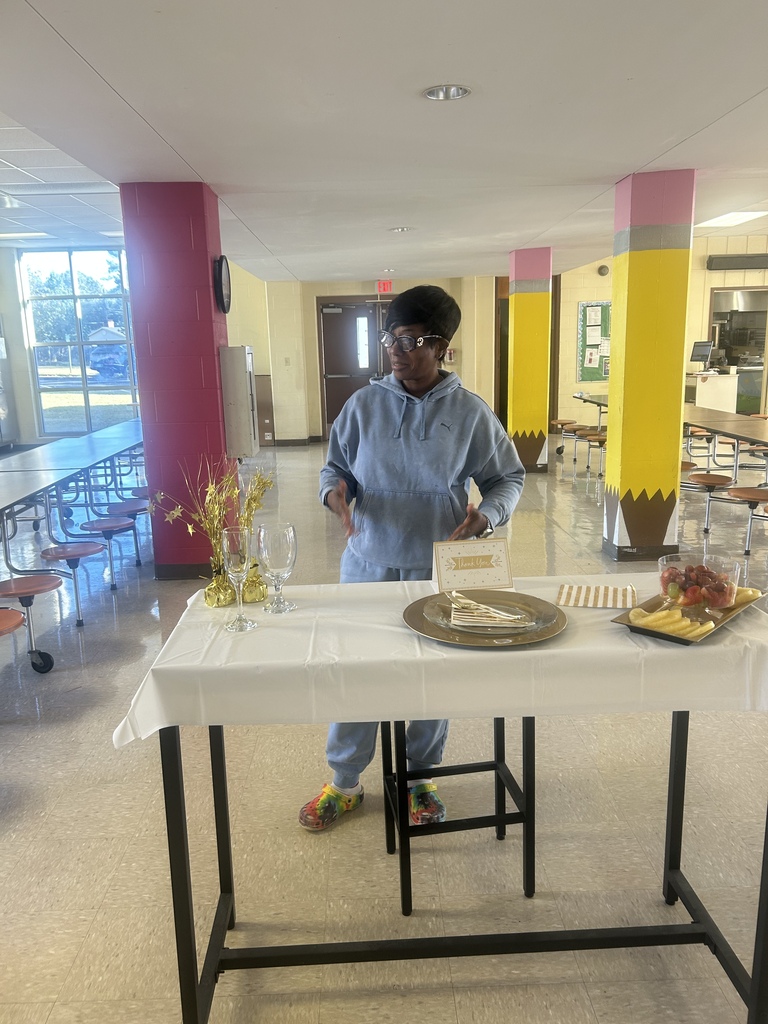 A person stands at a table with a white tablecloth. There are plates, glasses, and flowers on the table.