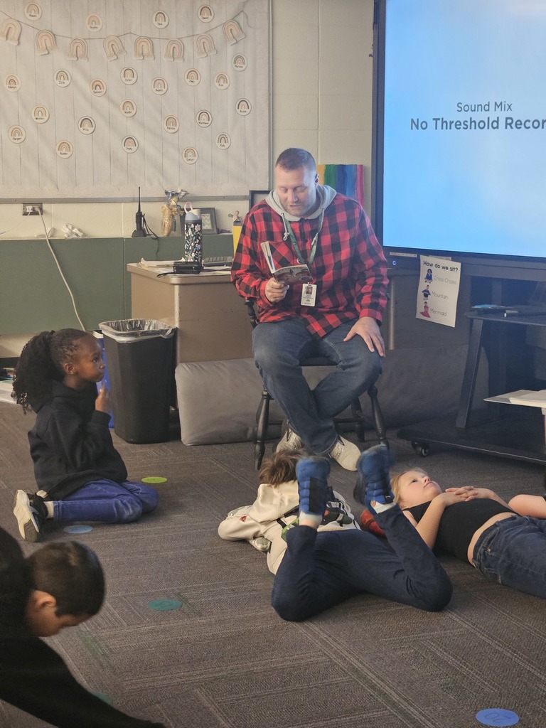 Educator in plaid sweatshirt reading aloud in the classroom for 3rd grade students in Pine City. 