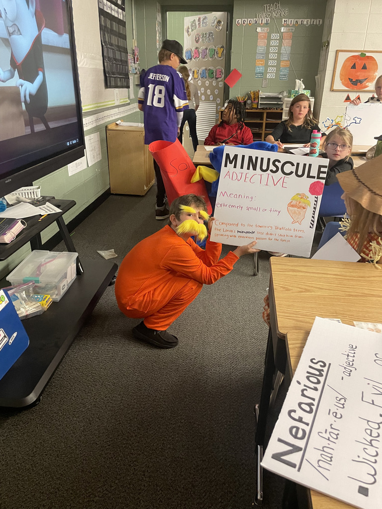 Orange costumed character with a vocab sign for minuscule