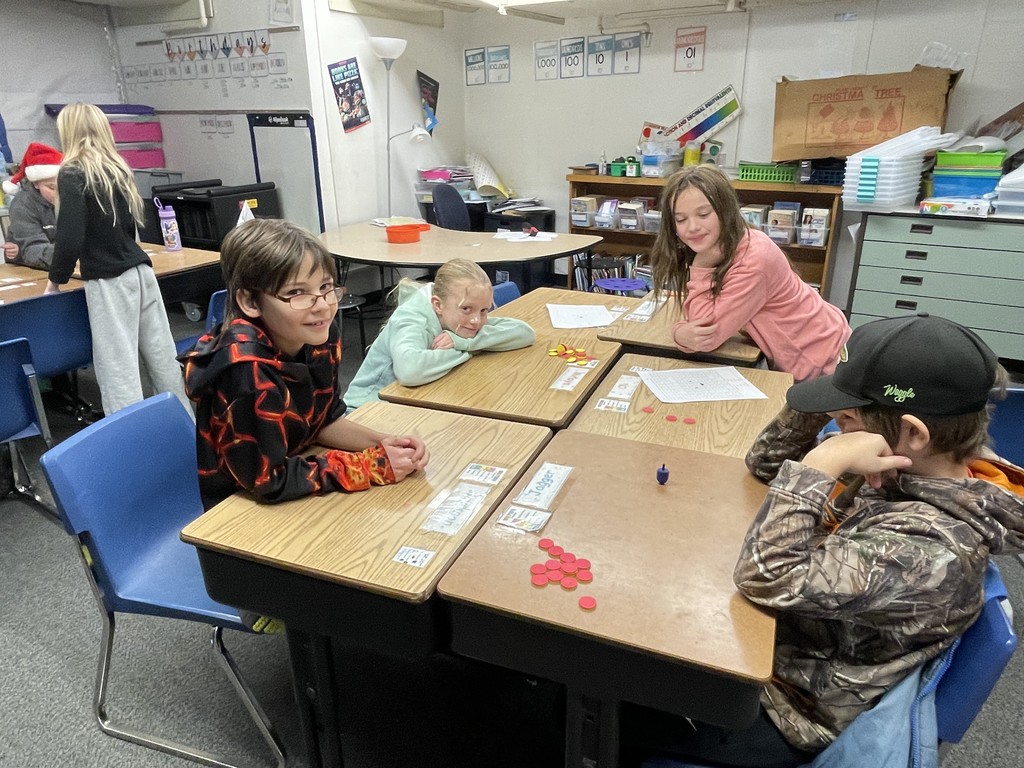 Four elementary students seated at desks playing a game during the holiday season.