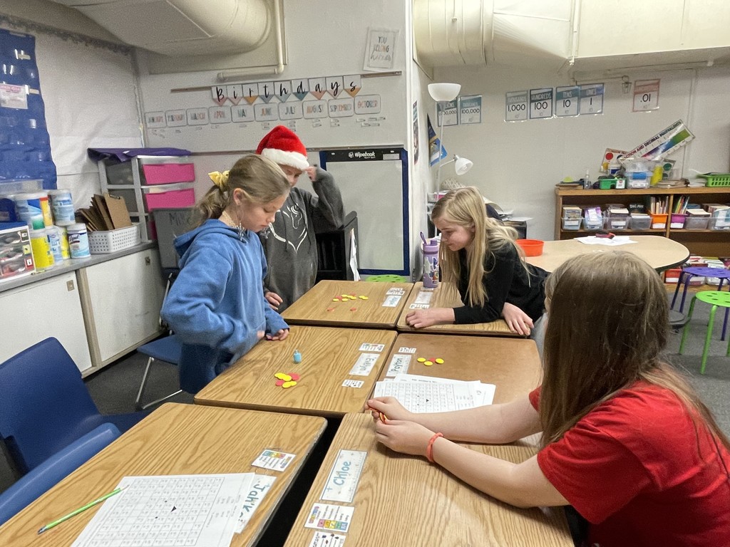 Four elementary students seated at desks playing a game during the holiday season.