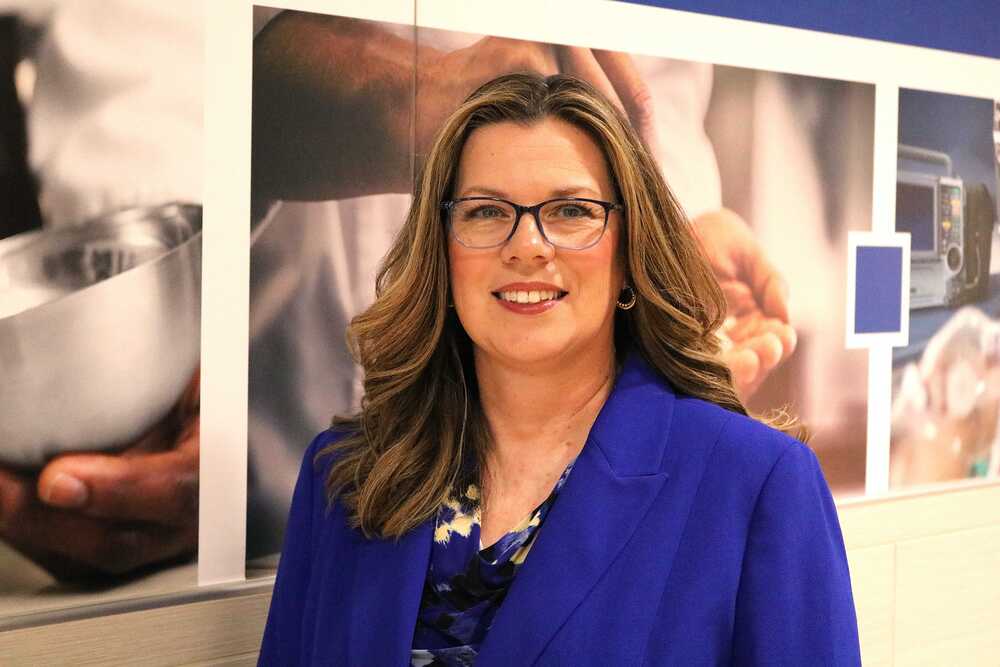 Pioneer Tech woman in blue blazer and glasses standing in front of mural