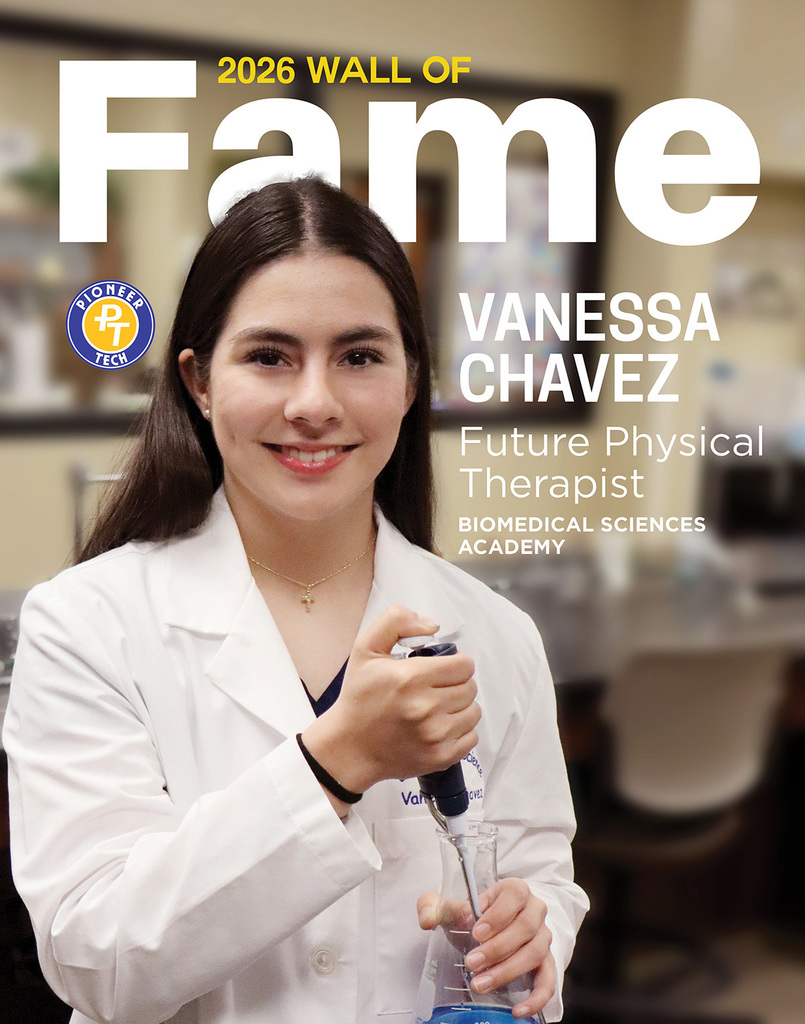 brown haired girl with lab equipment in white coat with wall of fame behind her. 