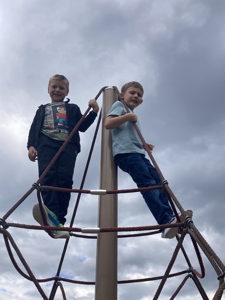 Two boys look down from a spiderweb like climber on the playground.