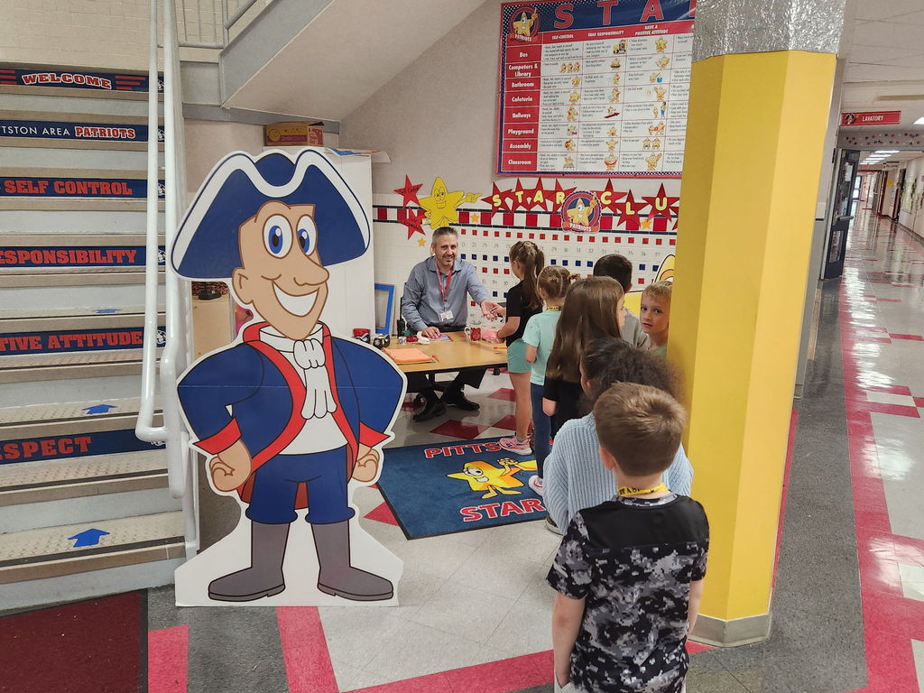 Students line up in the hallway to receive their first STAR tickets from the principal. A colorful Patriot mascot cutout and the STAR behavior chart are displayed proudly nearby.