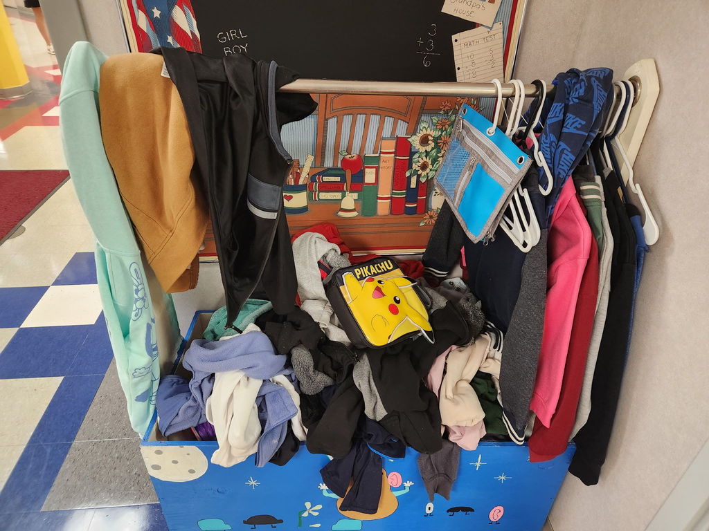 A large lost and found caddy draped with children's sweaters, pencil cases and a pikachu lunch box.