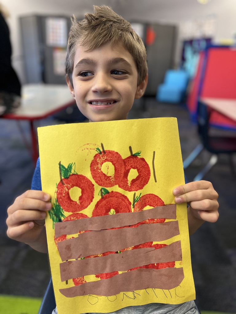 A boy holding a basket of apple painting smiling at the camera. 