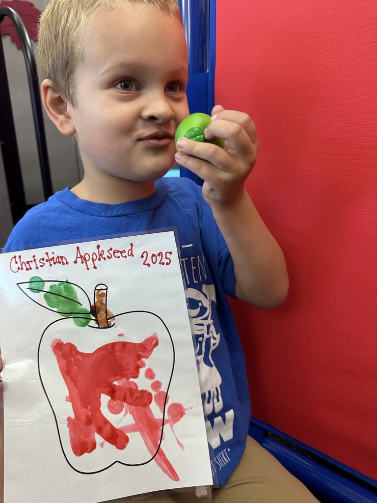 A boy holding an apple coloring sheet with red, broen, and green dots while smelling an apple foam toy.