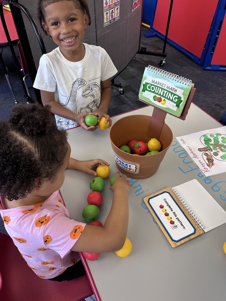 A boy smiling at the camera holding apple math manipulatives while a girl creates apple patterns  with apple math manipulatives.