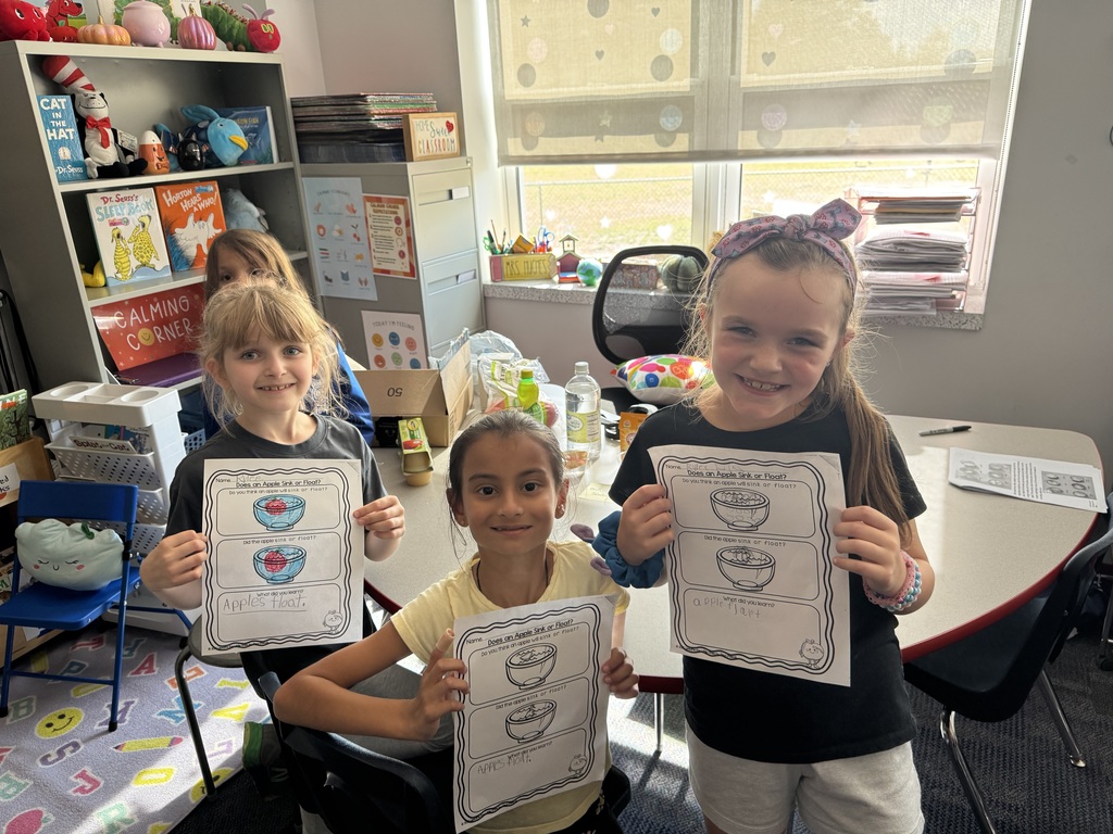 Girls in a classroom holding sink or float apple activity sheets