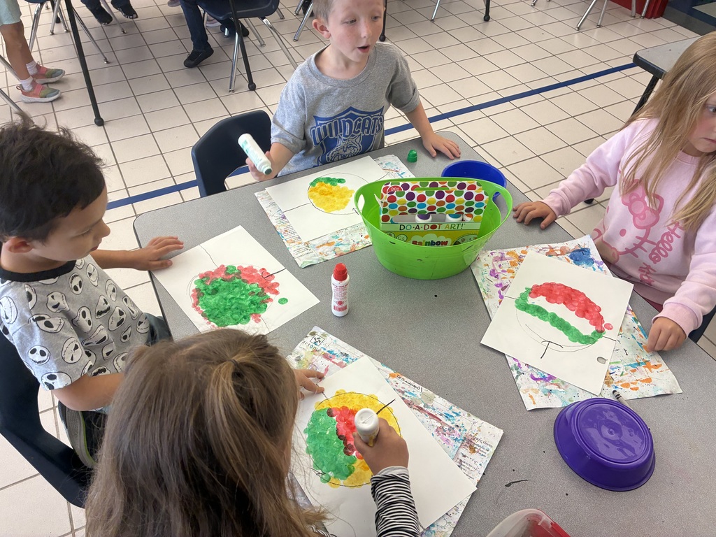 Students at an art table using red, yellow and green dot markers to color their apple drawings