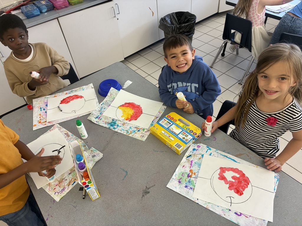 Students at an art table using red, yellow and green dot markers to color their apple drawings