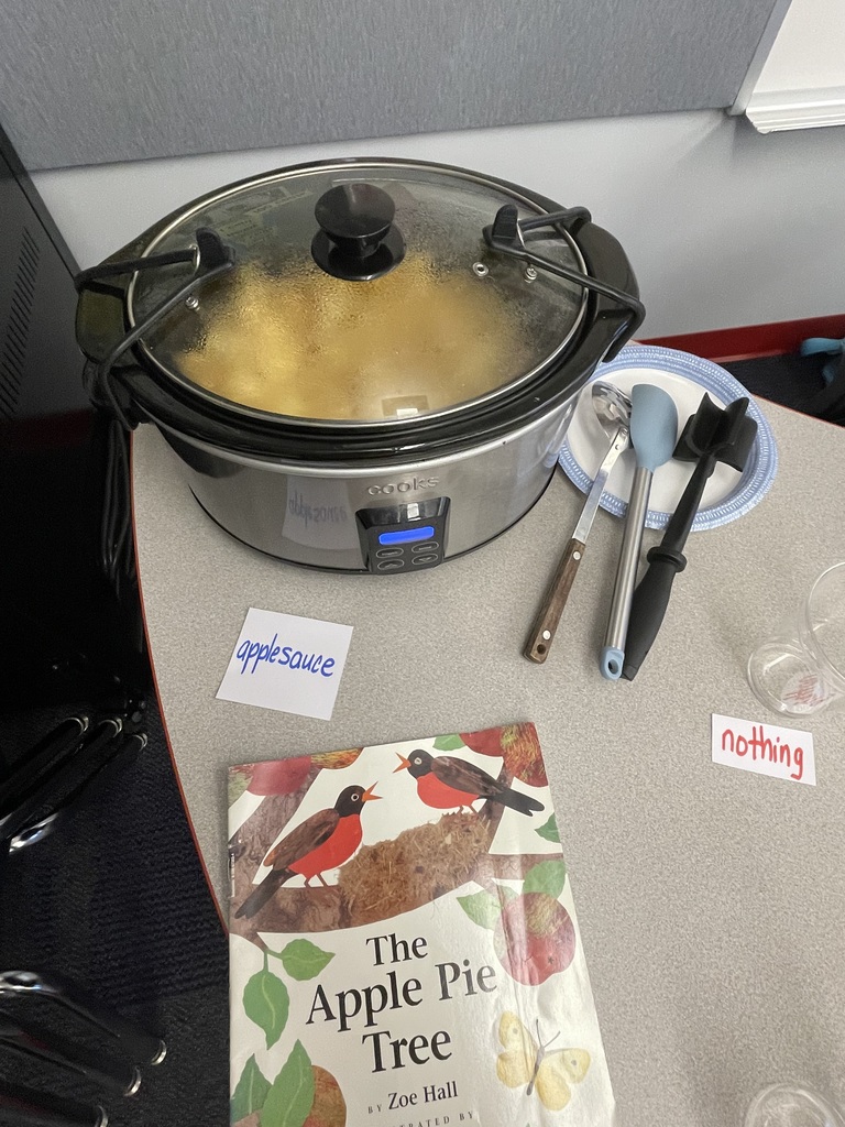 A classroom table with a crock pot labeled apple sauce and a book The apple pie tree