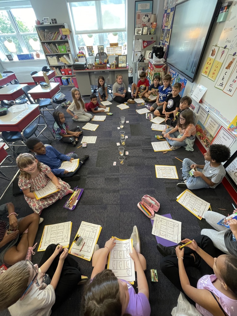 A class seated in an oval around and apple experiment with papers to document their findings