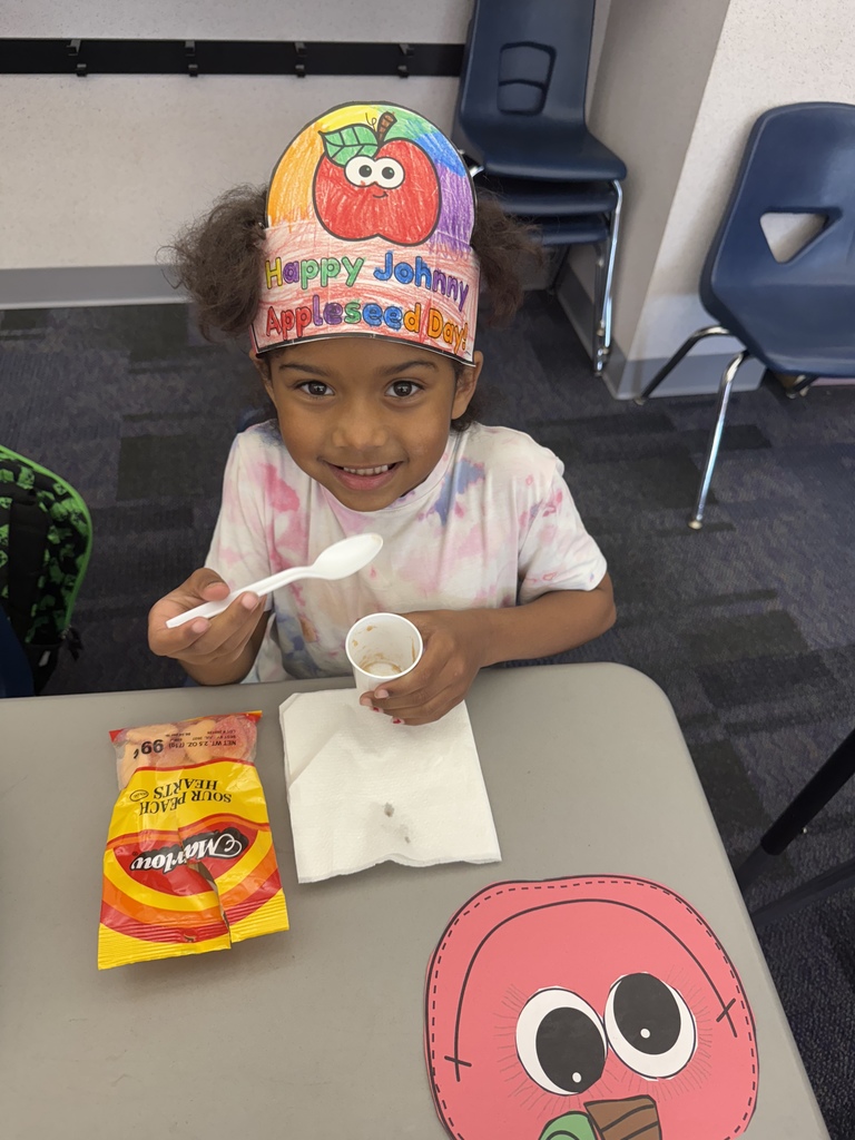 A student smiling eating homemade apple sauce and an apple craft on their desk. 