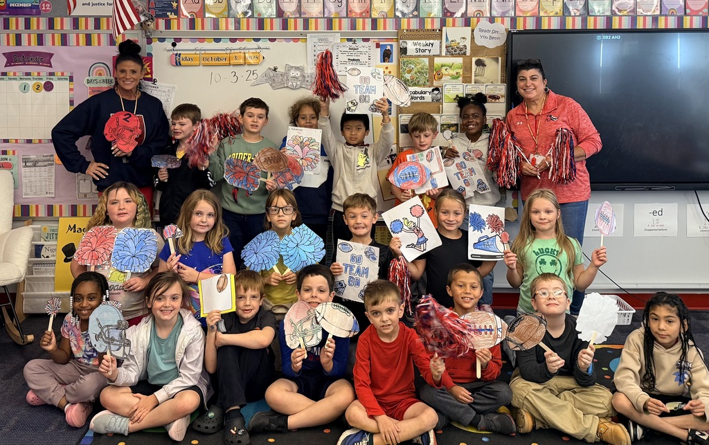 Students in a classroom with two teachers holding handmade photoball signs and pom poms