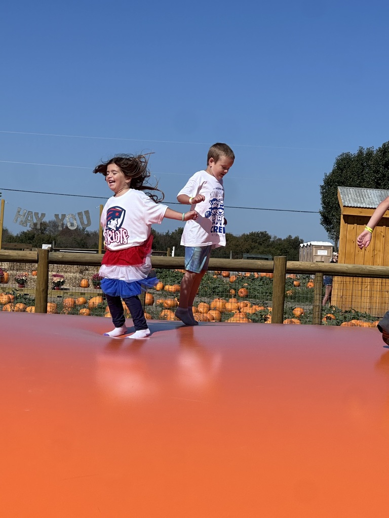 A boy and a girl jumping on an inflatable with pumpkins in the background.