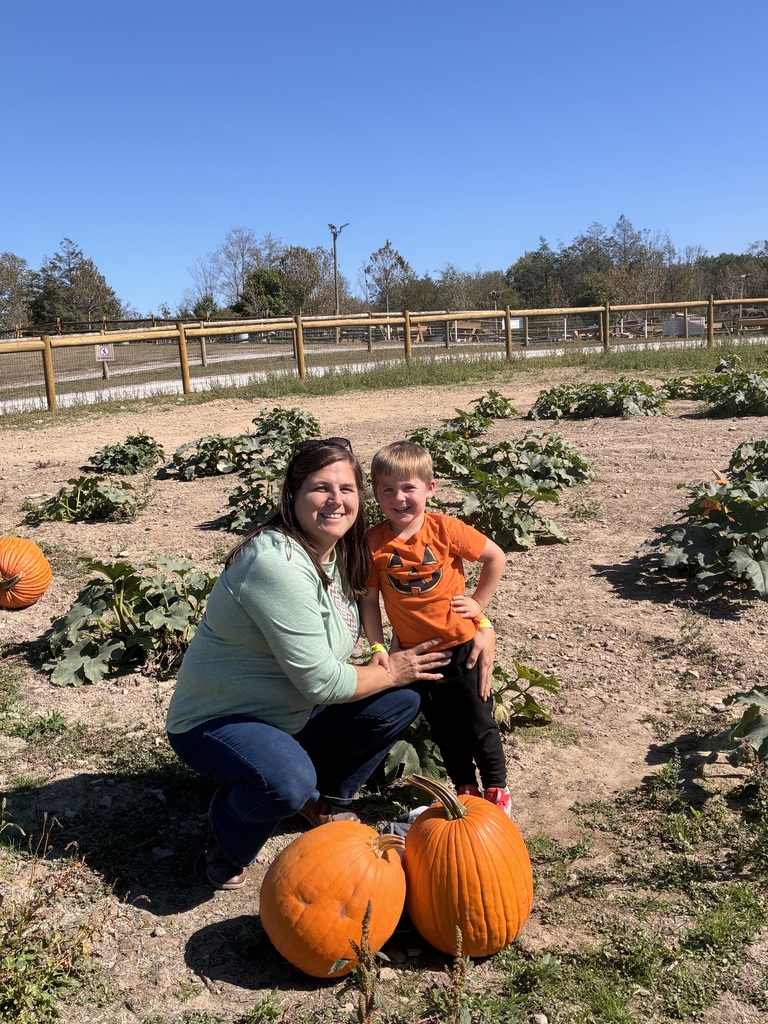 A boy and his mom smiling in a pumpkin patch.