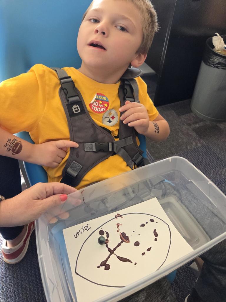 A boy with a football paper in a tupperware with brown paint.