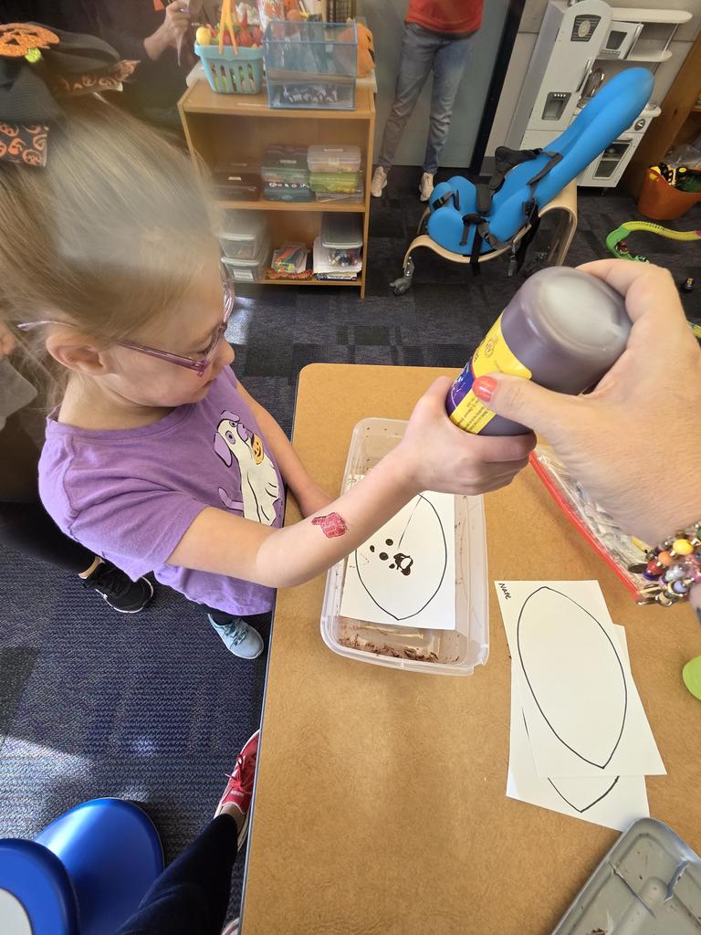 A girl squeezing brown paint on a football outline.