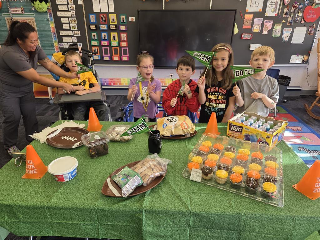 A group of students holding red white and blue football signs in front of a football decorated table with food.