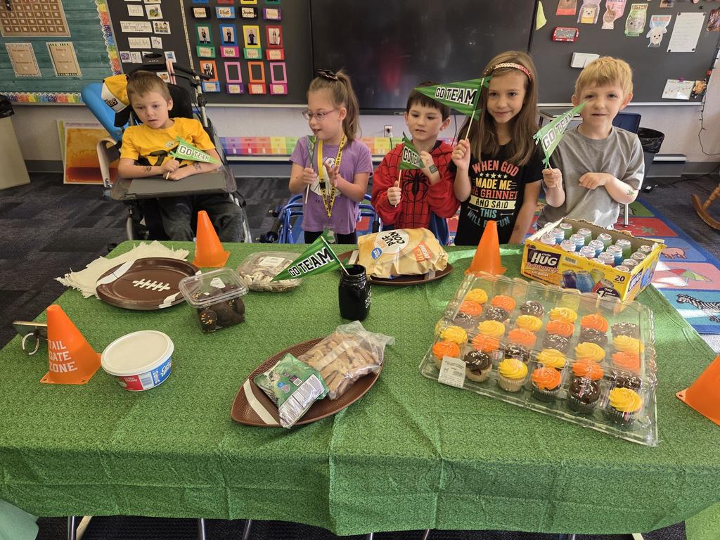 A group of students holding red white and blue football signs in front of a football decorated table with food.