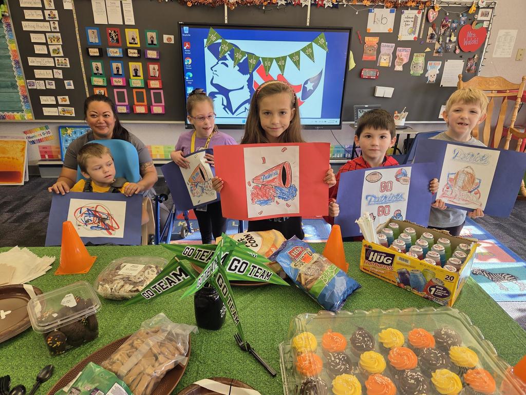 A group of students holding red white and blue football signs in front of a football decorated table with food.