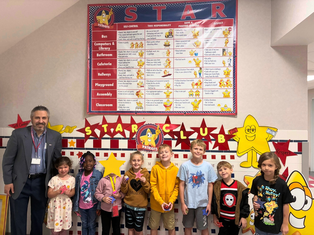 A group of 8 students and Mr. savokinas smiling in front of the star bingo board.
