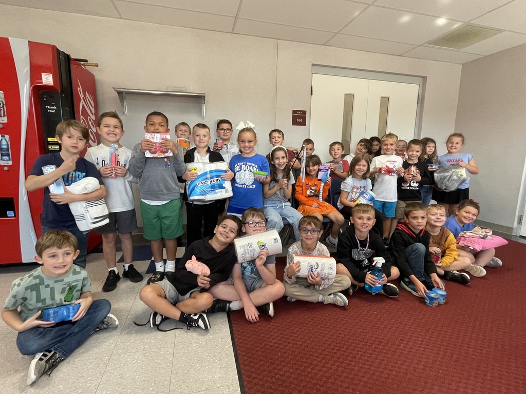 A group of students smiling at the camera holding donated items such jas paper towels, cleaning supplies and dog treats.