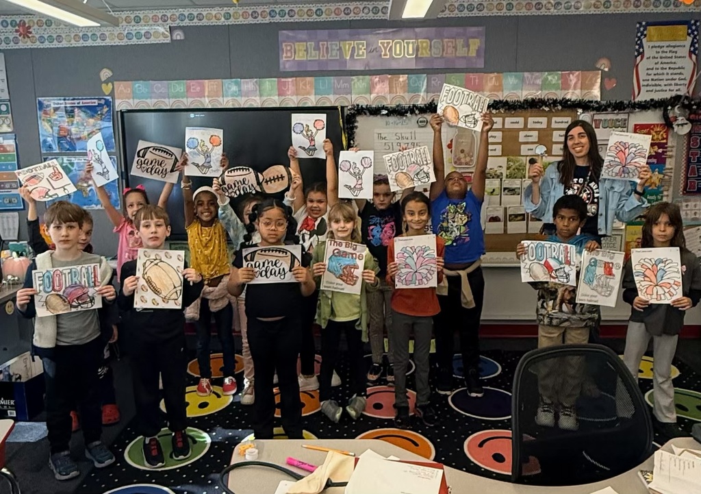 Students in a classroom holding red white and blue coloring pages with footballs and cheerleaders.