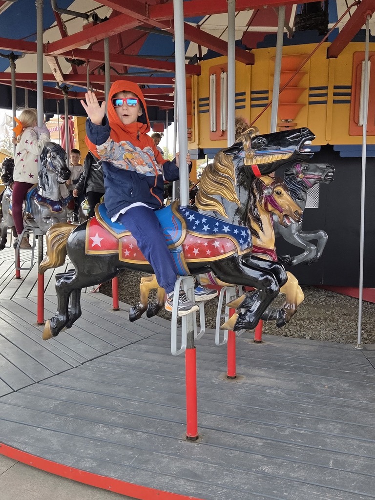 A kid on a carousel smiling.