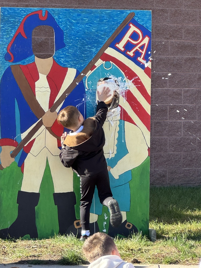 A boy hitting his teacher with a whip cream pie in a patriot cutout.