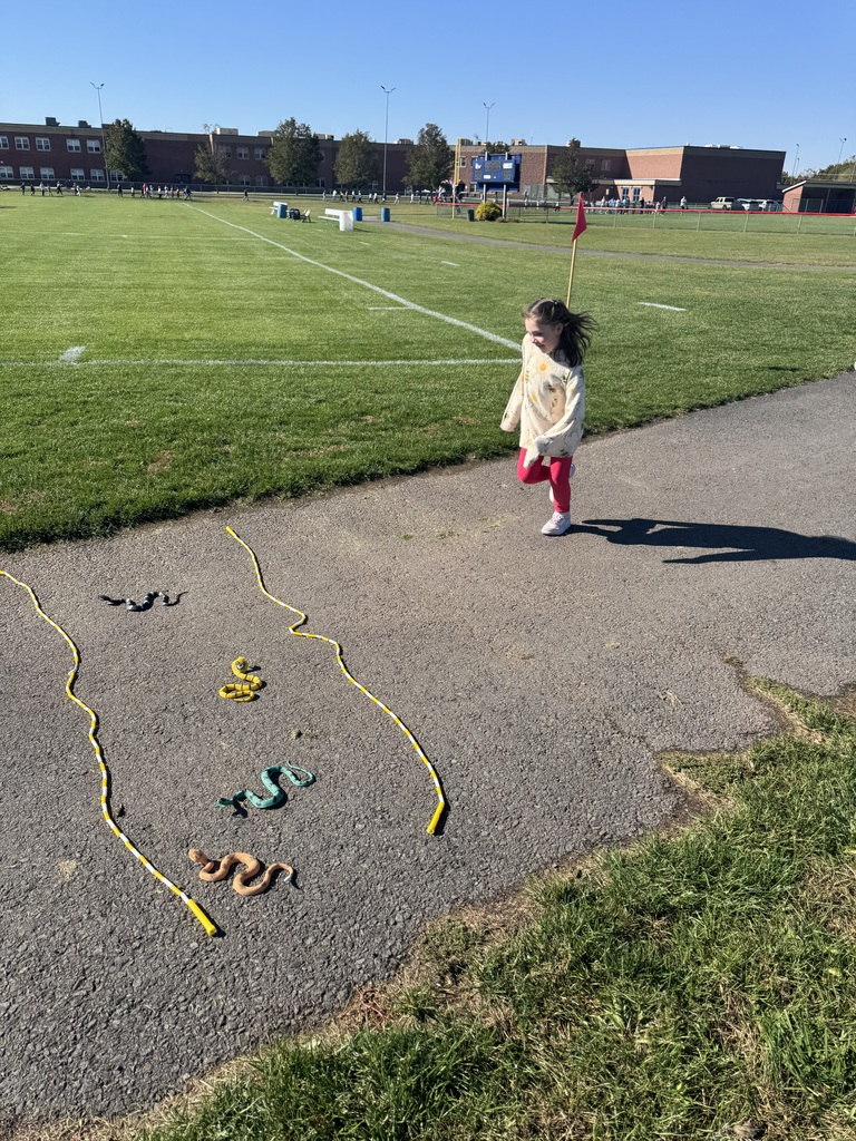 A girl jumping over two yellow jump ropes and plastic snakes on an outdoor track.