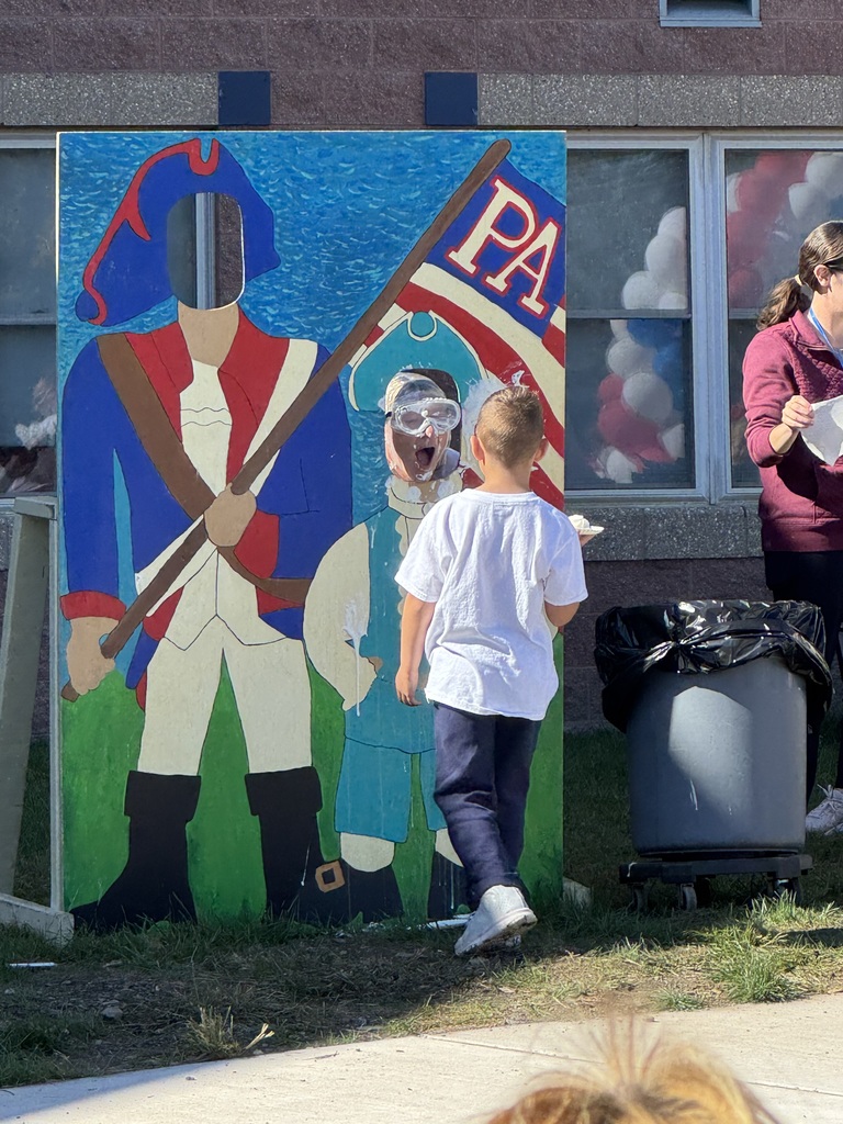 A boy throwing a whip cream pie at a teacher in a patriot cut out.