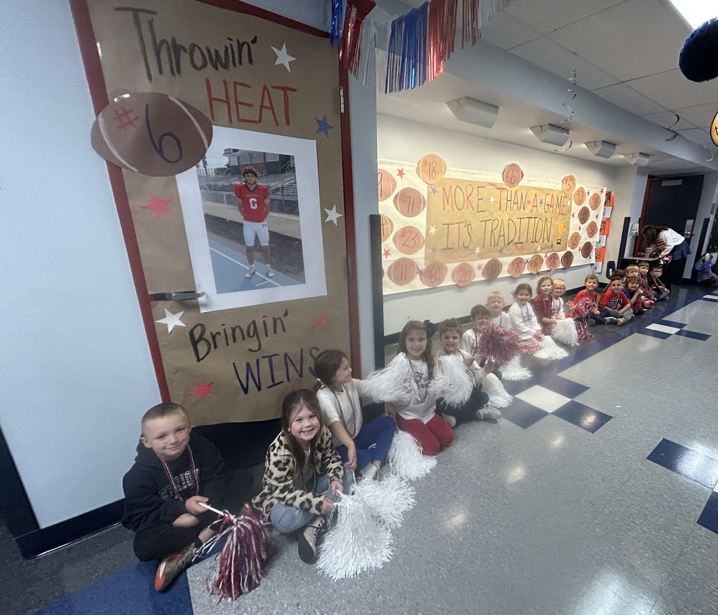 Students sitting in a hallway with pom poms with football signs behind them.