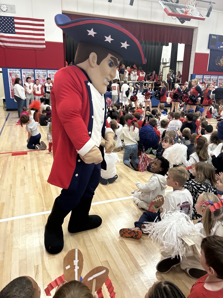 Patriot mascot in a gym filled with students and teachers at a pep rally.