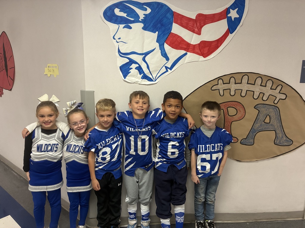 Wildcat football players and cheerleaders smiling at the camera in the school hallway.